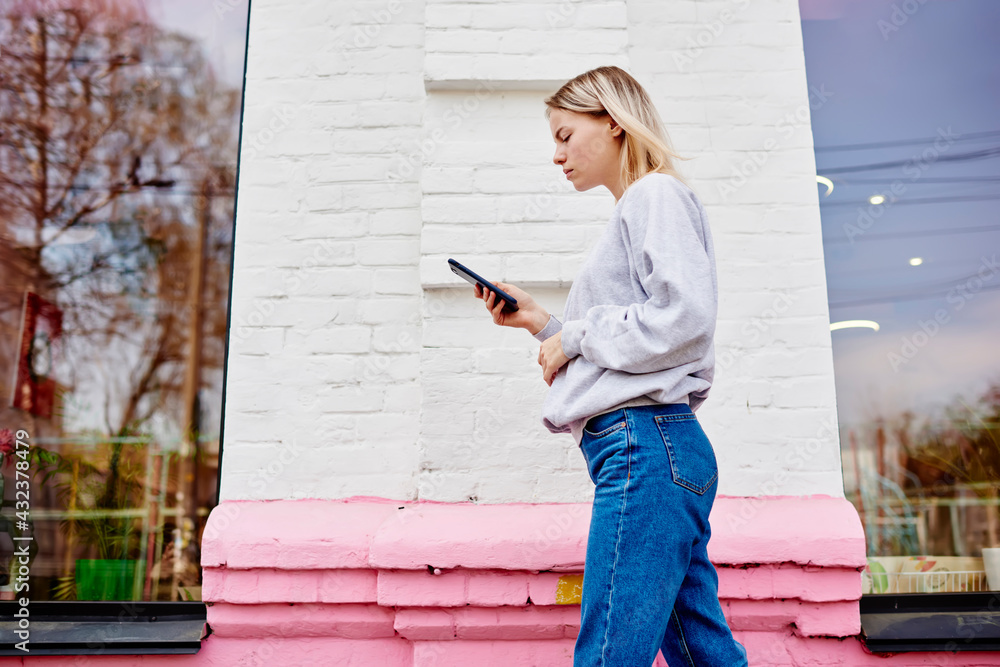 Poster caucasian hipster girl sending sms via mobile application using 4g wireless internet while walking i