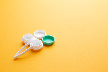 Accessories for contact lenses: a container for lenses and tweezers on a yellow background