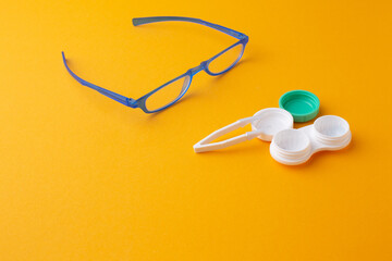 Glasses and accessories for contact lenses: a container for lenses and tweezers on a yellow background