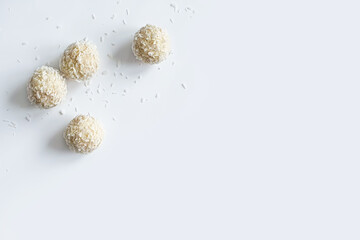 White Chocolate candies with coconut crumb and coconut confectionery flakes on white background. Handmade candies, Sweet balls concept. Copy space in right side. Top view. Selective focus.