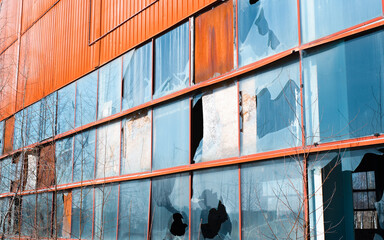 Facade of an abandoned warehouse outside during the day. Broken glass, rust, crumbling foundations.