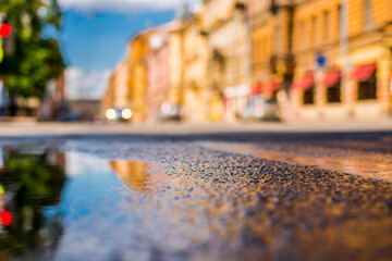 Obraz premium Sunny day after rain in the city, the headlights of the approaching car on the road. Close up view from the level of the puddle on the pavement