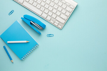 Working blue table with keyboard, notebook, pencil, stapler and paper clips. Space for your inscription - obrazy, fototapety, plakaty