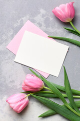 Greeting card mockup with pink envelope and tulip flowers on grey concrete background