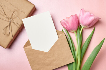 Greeting card mockup with gift box, envelope and tulip flowers on pink background