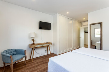 Clean and simple looking bedroom with a double bed facing a TV, small table stand and chair. With great daytime lighting.