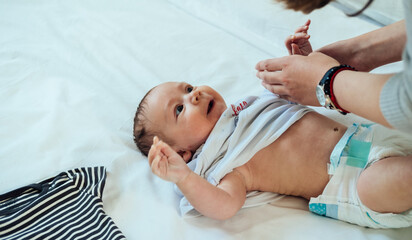 Mother Dressing Up Little Baby in Bed.
Close up photo of adorable baby boy baby lying in bed and...