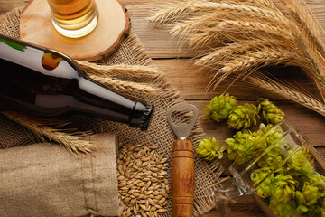 A bottle of beer with green hops, oat, wheat spikelets, opener and glasses with dark and light beer...