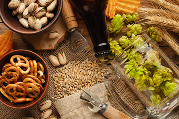 A bottle of beer with green hops, oat, wheat spikelets, opener and glasses with dark and light beer...