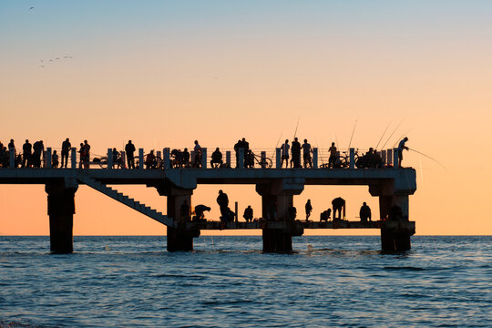 Silhouettes of the people fishing and enjoying the sunset over sea on a pier