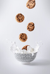 chocolate chip cookies, falling into white milk with splash on white background, vertical, cold and light colors