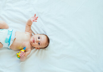 Portrait of Cute Baby Looking at Camera and Holding Rattle Toy in Hand on White Sheets with Copy...