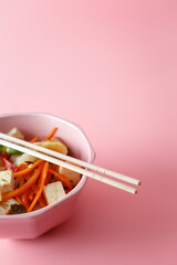 
Udon noodles with oyster sauce, chicken and vegetables in a pink plate on a pink background. Modern Asian food concept. Wooden chopsticks
