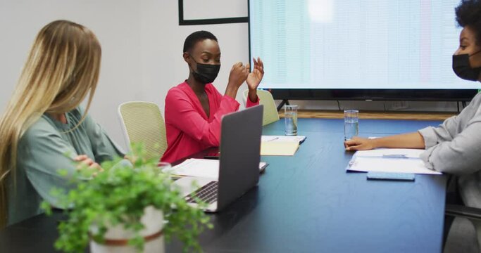 Three diverse businesswomen wearing face masks in discussion at an office meeting