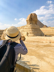 A girl in a straw hat takes pictures of Sphinx in Giza - 432389880