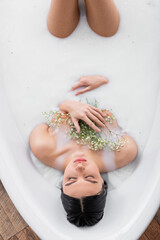 overhead view of pretty woman with gypsophila flowers enjoying bathing in milk.