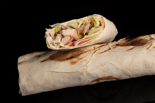 Classic shawarma kebab pita with chicken and vegetables and sauce on a black background. in section