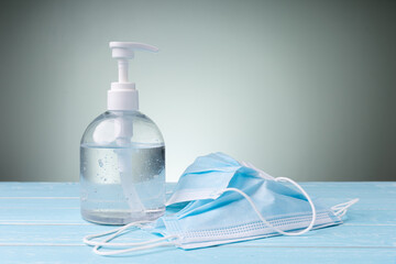 The bottle alcohol gel and medical mask on blue table with copy space behind is green background. Everyone needs to wash their hands frequently, wear medical masks.