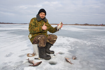 A joyful European man holds a caught fish in his hands. A male fisherman catches fish on the ice of a lake.