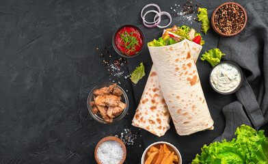 Shawarma with vegetables, salad and chicken on a black background with ingredients.
