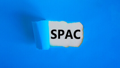 SPAC, special purpose acquisition company symbol. Words 'SPAC' appearing behind torn blue paper. Beautiful blue background, copy space. Business and SPAC, special purpose acquisition company concept.