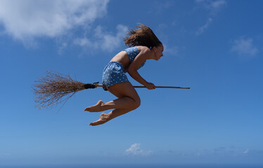 Caucasian woman flying on the broom as a witch on sky background