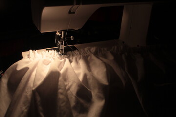 gathered white fabric under sewing machine foot. dim warm light at night