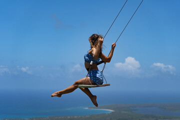 Young beautiful caucasian woman on the rope swing with sea and sky background. Concept of Vacation...