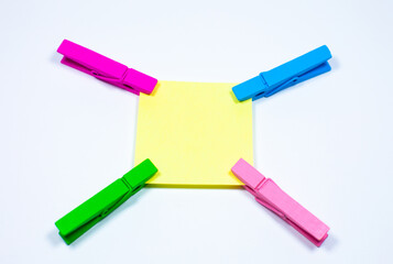 Blank yellow sticker with colorful wooden clothespins. Close up of note paper on white background. Copy space.