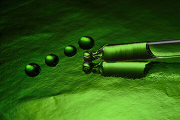 a cosmetic pipette with liquid lies on a green background covered with drops. close-up.