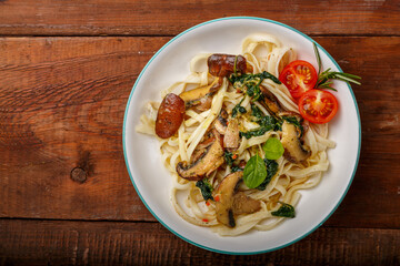 Udon with mushrooms and spinach in a plate on a wooden table.
