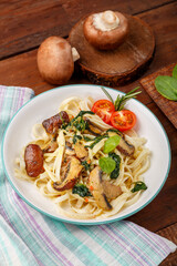 Udon with mushrooms and spinach and cherry tomatoes in a plate next to greens.