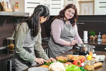 Two young cheerful girlfriends preparing meal together in the home kitchen.
