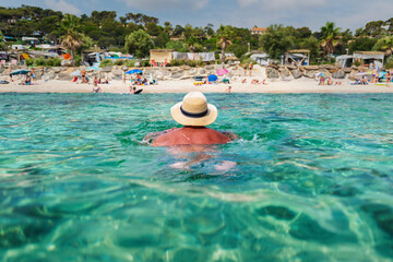 Fototapeta na wymiar man with hat swimming relaxed in azure water with view on beach
