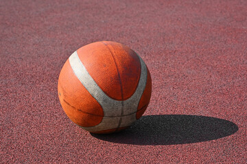 Orange basketball ball on red outdoors court