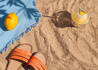 Fototapeta na wymiar Bright summer beach vacation or travel lifestyle concept flat lay with lemonade and a flip flops on the sand. Top view 