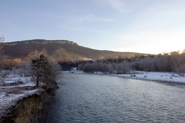 Winter in the foothills, an ice-free river on a frosty morning in the rays of the rising sun.