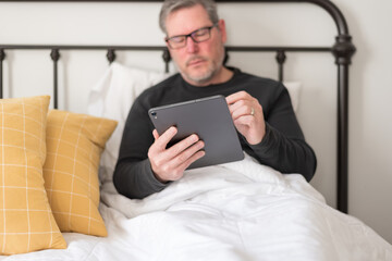 Man using a digital tablet while sitting in bed