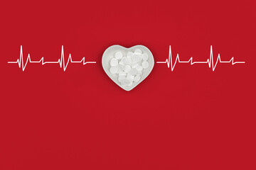 Medical concept with heart shaped plate, pills and cardiogram heart rate beats on red background