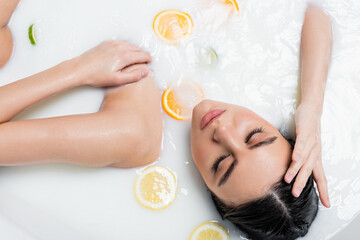 top view of young woman in bath with milk and sliced citrus fruits.