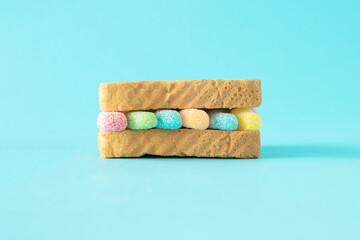 Colorful soft gummy candie between two pieces of toast . Light blue background.