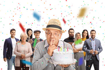 Elderly man holding a birthday cake for a surprise party with people behind