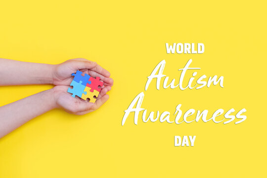 Autistic pride day. The hands of a small child holding colorful puzzles on yellow background. Heart of puzzles. Banner