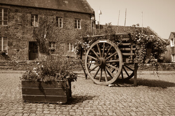 Fototapeta na wymiar Brittany, France. Wooden carriage decorated with flowers at the square of the medieval village Locronan. Sepia historic photo.