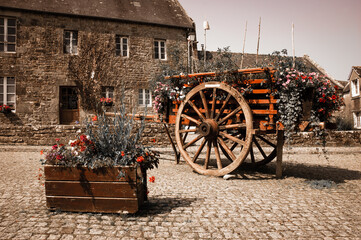Fototapeta na wymiar Wooden carriage decorated with flowers at the square of the medieval village Locronan. Brittany, France. Vintage toned photo.
