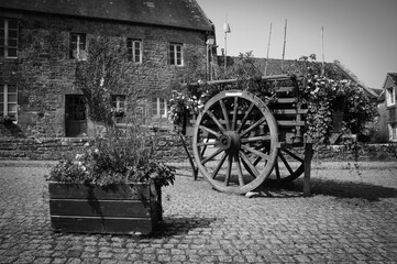 Fototapeta na wymiar Wooden carriage decorated with flowers at the square of the medieval village Locronan. Brittany, France. Black and white historic photo.