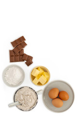 Baking ingredients - eggs, butter, flour, chocolate and sugar on white background, view from above