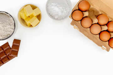 Baking ingredients - eggs, butter, flour, chocolate and sugar on white background, view from above