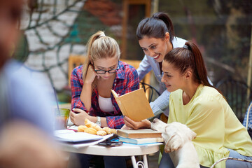 A group of female students reading an interesting book while sitting in a bar. Leisure, bar, outdoor, friendship