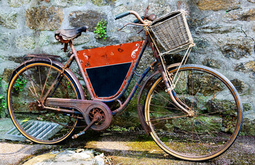 Fototapeta na wymiar Rusty vintage bicycle with black board for entering a text (advertisement, menu etc) and wicker basket leaning on a stone wall. Brittany, France.